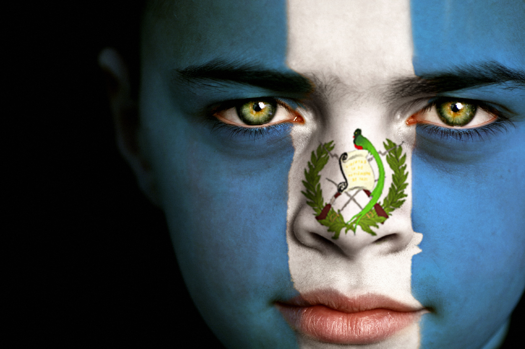 Portrait of a boy with the flag of Guatemala painted on his face.