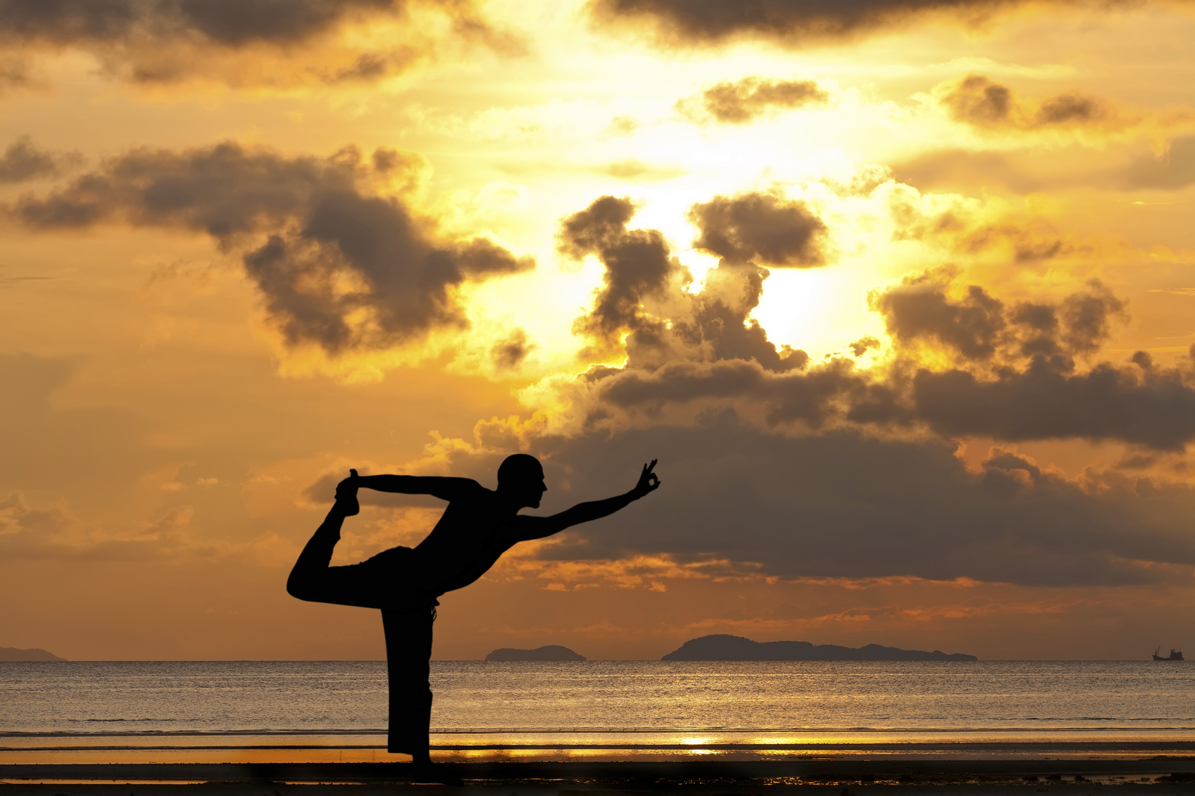 Man silhouette doing yoga exercise natarja at sunset beach