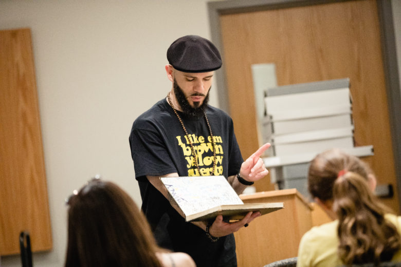 Curator Ben Ortiz teaching class at Cornell University (2018, photo by Allison Usavage), holding a Graffiti blackbook by Quik, ca. 1983 — Cornell Hip Hop Collection 